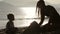Silhouette of mother and small daughter building sand castles on the beach