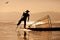 Silhouette of Myanmar fisherman on wooden boat at sunset .Burmese fisherman on bamboo boat catching fish in traditional