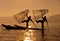 Silhouette of Myanmar fisherman on wooden boat at sunset .Burmese fisherman on bamboo boat catching fish in traditional