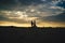 Silhouette of newlyweds on evening beach. Bride and groom walking on horizon. Dramatic sky with sun rays among clouds in