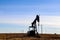 Silhouette of oil-gas pump jack out in field behind barbed wire fence silhouetted against blue sky with whispy clouds - with elect