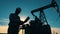 Silhouette of an oil worker and an oil pump. Oil industry, crude oil prices concept.