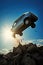 silhouette of a old generic silver blue car crashing flying off a cliff. Stone cliff. Blue sky. White clouds. Car accident.