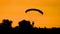 Silhouette of parachutist flying on parachute in golden sky during sunset in summer.