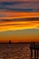 Silhouette of people taking pictures of a sailboat under fire-like clouds reflected in ocean