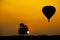 Silhouette of the people, tree and hot air balloon on a colorful sunset with big sun in background and copy space