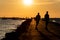 The silhouette of the people walking and skateboarding on the pier. Evening pastime.