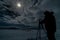 Silhouette of a photographer, photo camera and tripod on a totally snowy esplanade with the full moon illuminated the cloudy night