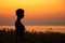 Silhouette portrait of a woman standing in the grass, in profile, headshot, in the rays of the setting sun over the sea