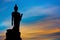 Silhouette Of The Posture Of Walking Buddhist Statue In Twilight