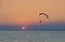 Silhouette of powered paraglider soaring flight over the sea against marvellous orange sunset sky.