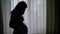 Silhouette Of Pregnancy Woman Stroking And Caressing Her Tummy Against A Window