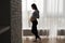 silhouette of a pregnant woman standing near a large window and stroking her big belly.