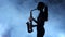 Silhouette professional musician female playing on saxophone. Smoky isolated studio