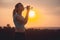 Silhouette profile of a beautiful girl drinking water after running a distance in a field at sunset, athletic woman with bottle