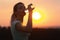 Silhouette profile of a beautiful girl drinking water after running a distance in a field at sunset, athletic woman with bottle