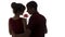 Silhouette profile of a young couple sensually bowed their heads to the bud of a rose on white isolated background, boy and girl