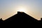 Silhouette of a pyramid-like house roof before the bright sky background