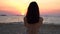 Silhouette rear view of young woman calmly sitting on the tropical beach in sunset evening. Lonely girl looking the