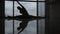 Silhouette and reflection of a young gymnast by the window. A girl in a twine is doing exercises by the window.
