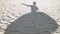 Silhouette on sand of a dancing girl in a dress fluttering in the wind.