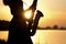 Silhouette of a saxophone in hands of young woman near the river at sunset
