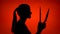 Silhouette of scary woman holding sharp blade. Female`s face in profile with knife on red background