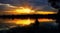 The silhouette of a seated fisherman on a beautiful background of a rising sun with rays in the dramatic clouds .