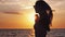 Silhouette of seductive girl with long hair wearing sunglasses enjoying the sunset on the beach in slow motion in windy