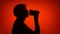 Silhouette of senior woman with coffee to go on red background. Female`s face in profile drink coffee