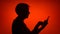 Silhouette of senior woman use cellphone on red background. Female`s face in profile browsing online