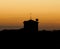 Silhouette shot of a small house with a stork nesting on the roof on top of a hill