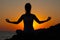 Silhouette of a slender fitness girl in the sun at sunset or sunrise in lotus pose.