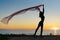 Silhouette slender girl at sunset on seashore rejoices with a transparent cloth