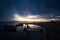 Silhouette of slim girl sitting on narrow wooden bridge at small motor boats at sunset