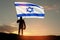Silhouette of soldier with Israel flag against the sunrise in the desert.