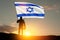 Silhouette of soldier with Israel flag against the sunrise in the desert.