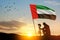 Silhouette of soldier kneeling with his head bowed against the sunrise or sunset and UAE flag. Commemoration Day.