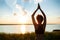 Silhouette of sportive girl practicing yoga in field at sunrise.