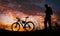 Silhouette of sports person cycling on the meadow on the beautiful sunset. Young man with camera and bicycle.