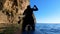 Silhouette of sportsman rowing SUP-board with paddle on sea water through shadow tunnel between old steep cliffs