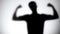 Silhouette of strong man showing biceps behind glass wall, bodybuilding concept