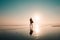 A silhouette of a surfer standing on a beach at sunset. With sun flare. Saunton, Devon, UK