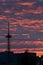 A silhouette of a tall telecommunication broadcasting tower against the vivid red sky on a cloudy summer evening