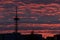 A silhouette of a tall telecommunication broadcasting tower against the vivid red sky on a cloudy summer evening