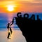 Silhouette teamwork of people climbs into cliff to reach the word GOAL sunrise (goal setting business concept)
