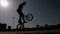 Silhouette of a teenage boy doing stunts on a BMX bike in a city Park.