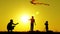 Silhouette of three unrecognizable people. Happy kids and father are playing with a kite at sunset. Education and