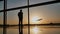 Silhouette of a tourist guy watching the take-off of the plane standing at the airport window at sunset in the evening