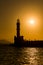 Silhouette of tourists on a Venetian harbor wall next to a lighthouse watching a spectacular sunset